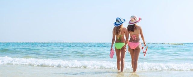 two women on beach in swimsuits looking out at the water